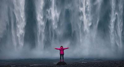 Person with arms outstretched in front of waterfall