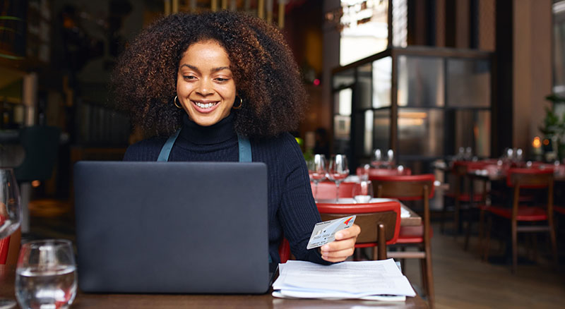 Person sitting at a cafe table with a laptop, card and papers