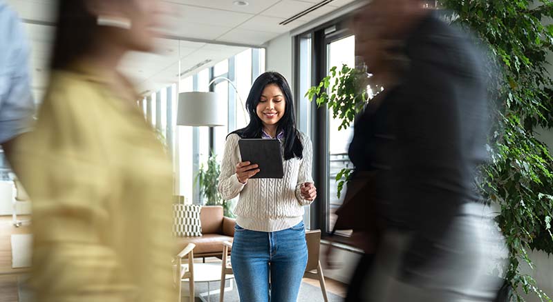 Person looking at a tablet while coworkers walk by