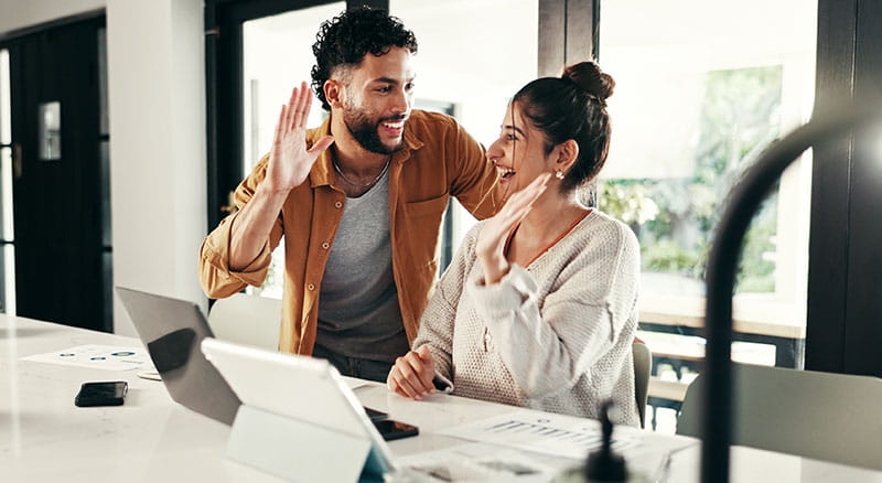 Couple high-fiving at home with papers and computer