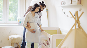 Pregnant woman with partner looking at crib in nursery