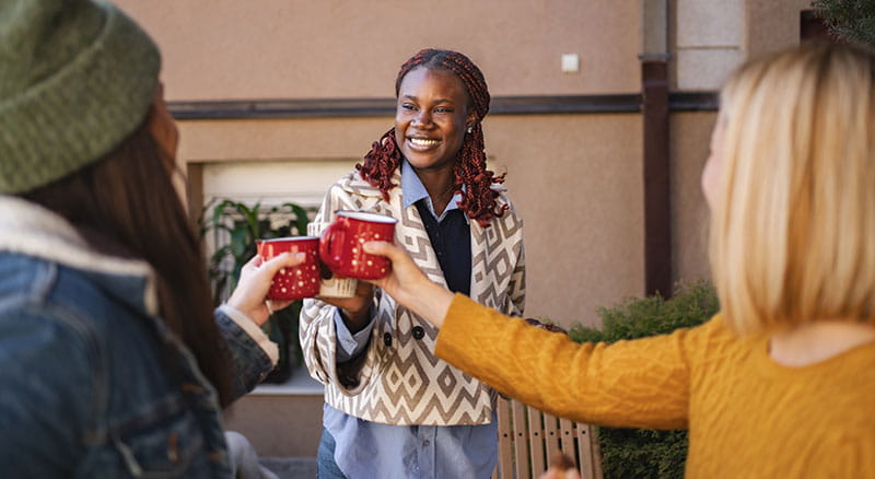 Three people cheering with mugs outside home
