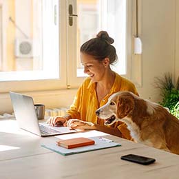 Person at laptop sitting next to a dog