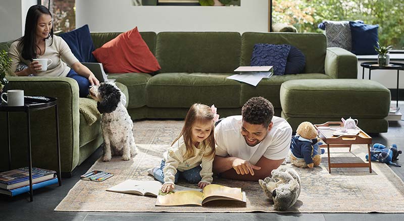 Father and daughter reading on the floor while a person pets a dog