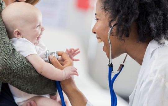 African American woman doctor with stethoscope checking heartbeat of baby being held by mom