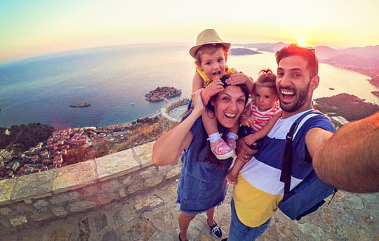 Family of four mom dad toddler son and daughter taking a selfie standing on a rock patio looking down on the ocean coastline