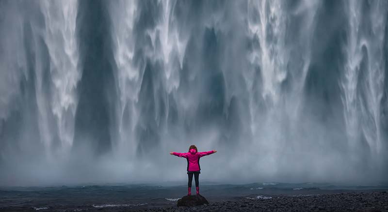Person with arms outstretched in front of waterfall