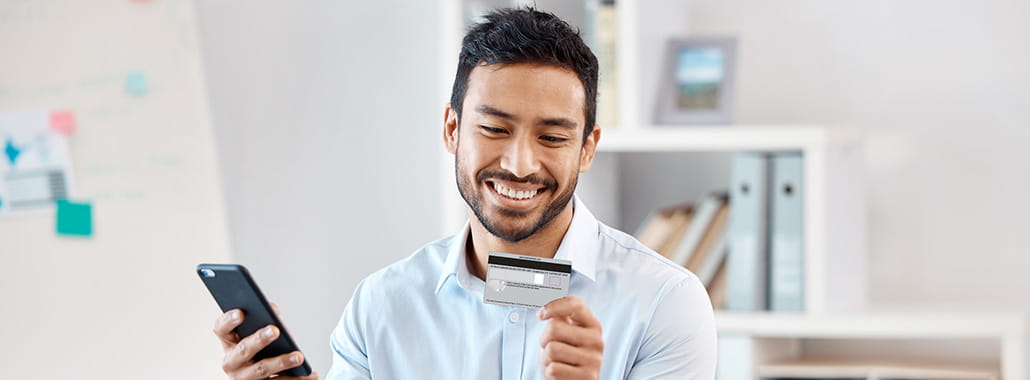 Person smiling while looking at credit card with phone in hand