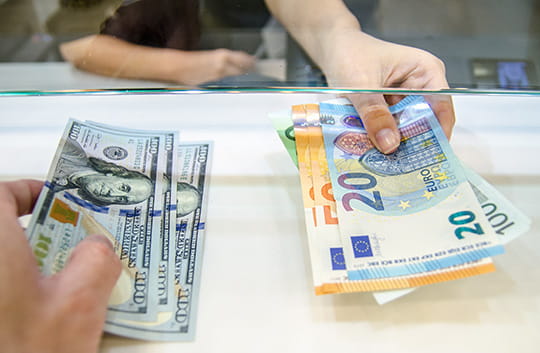Person holding US dollars and another person holding Euros
