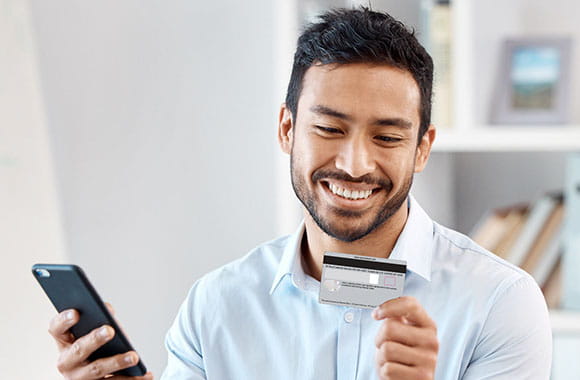 Person smiling while looking at credit card with phone in hand