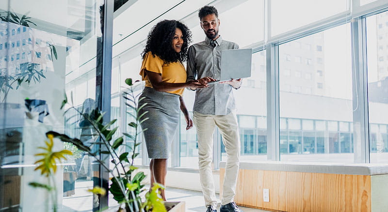 Two people walking in office looking at a laptop