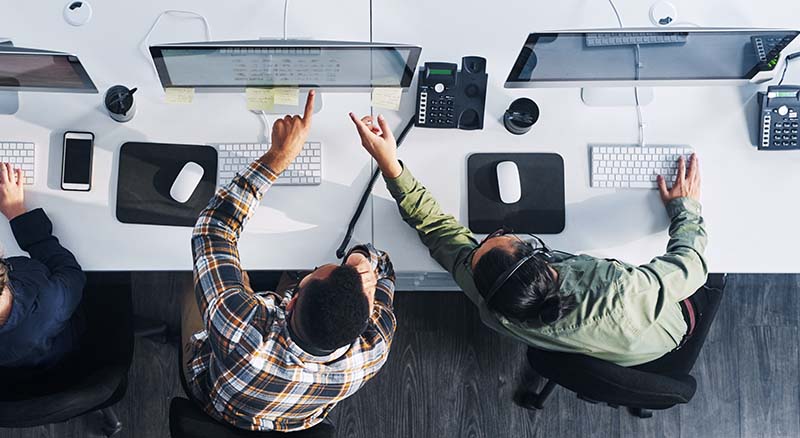 Two people looking at each others computers while on the phone in an office