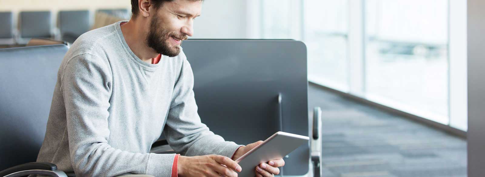 Man sitting in airport opens business bill pay with business online banking using a tablet