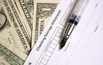 One dollar bills fanned out with a deposit slip on top of the cash and a fountain pen on top of the deposit slip