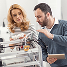 Dark haired man and blonde haired woman working on a 3D printer