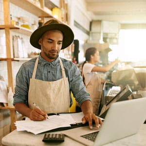 Business owner compares printed worksheets to information on laptop