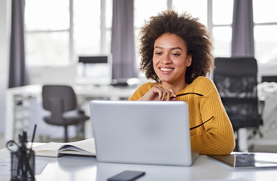 A woman takes off her glasses to look at her laptop