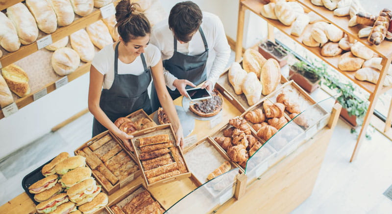 Woman and man behind the counter of their bakery shop accessing their Merchant Services account with Banner Bank.