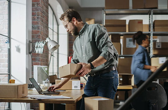 Business owner on laptop in busy warehouse