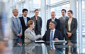 Group of business people in two groups each group has four people three standing and one person seated in each group the people seated are shaking hands