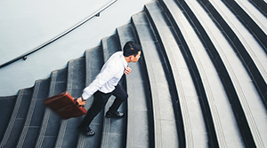 Man with dark hair in business attire walking up stairs carrying a briefcase