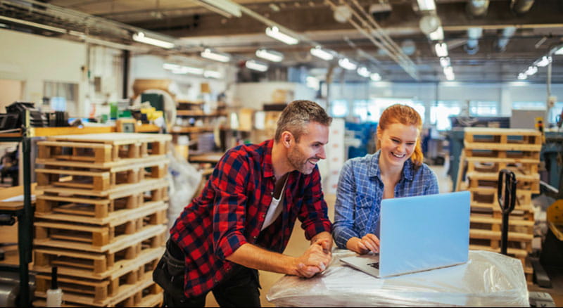Man and woman in warehouse look at laptop screen together