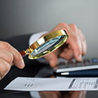 Caucasian male hands holding a magnifying glass examining a statement and the other hand is on a calculator