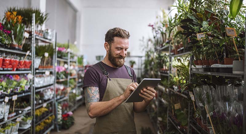 Person looking at tablet surrounded by racks of plants