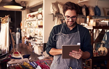 Caucasian male shop owner with brown hair, short beard and glasses wearing an apron holding a tablet