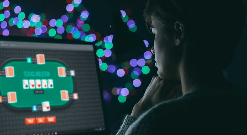 Woman playing computer poker in the dark with dots of blue, green and purple lights in the background.