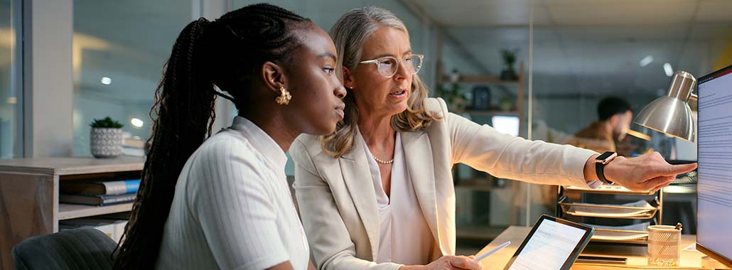 Two people at a desk pointing at a computer