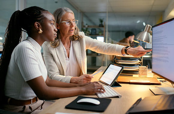 Two people at a desk pointing at a computer