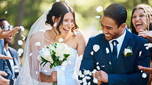 Bride and groom walking through thrown rose petals and smiling