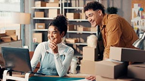 Two people surrounded by boxes looking at computer