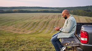 Person looking at phone while sitting on the back of a truck near a field