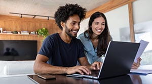 Two people looking at a computer and smiling with document in hand