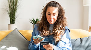 Person on couch looking at phone with card in hand