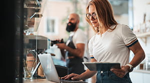 Person on laptop and holding tablet in cafe