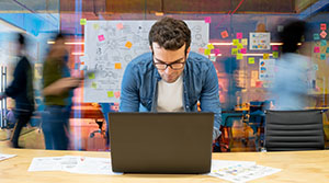 Person on computer in a busy office with post it notes in background