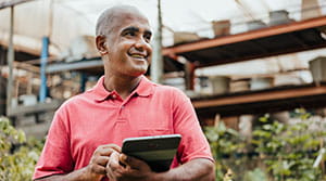 Person smiling with tablet in hand and plants in background