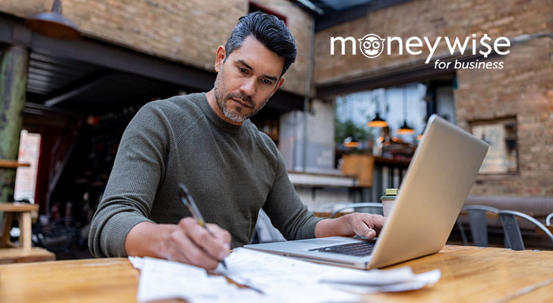 Person writing on paper with laptop and moneywise logo
