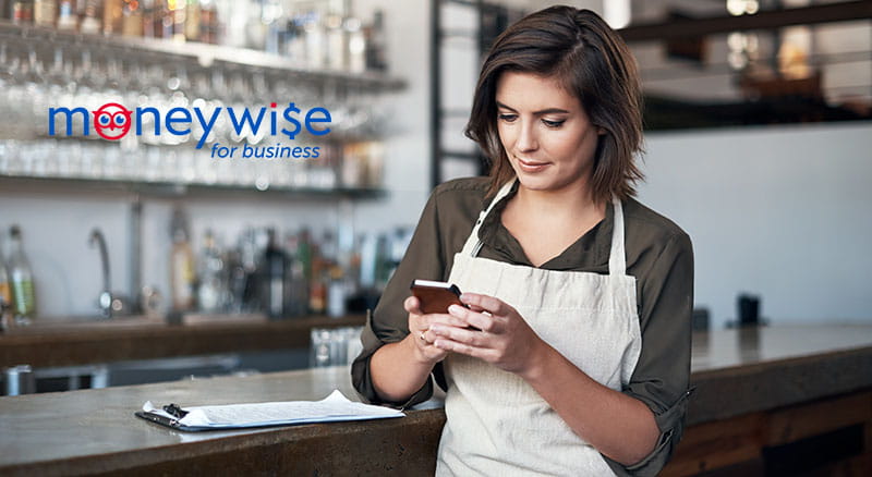 Person in restaurant looking at phone with MoneyWise logo