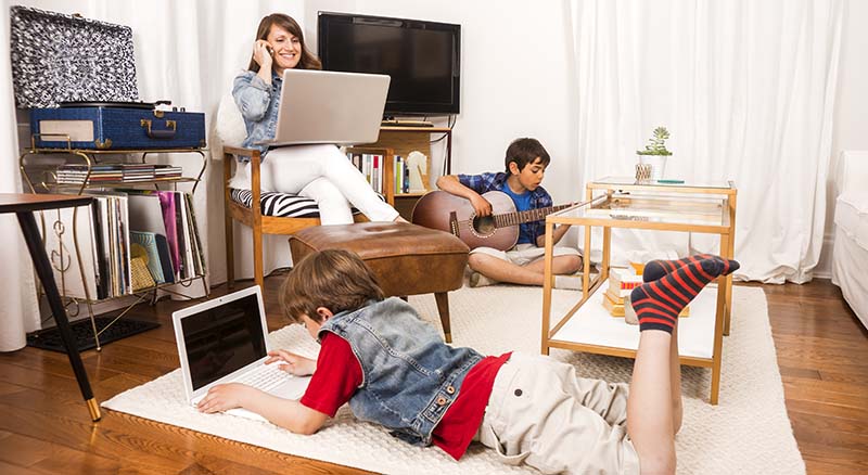 Person on the phone at a computer while a child plays a guitar and another is on the floor