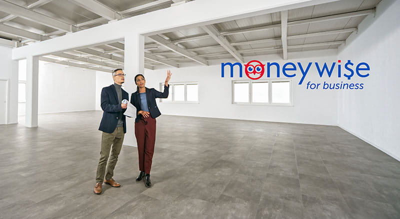 Two people pointing in an empty office space with MoneyWise for business logo