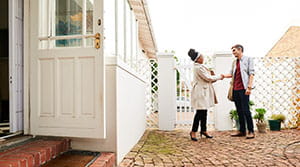 Two people shaking hands outside of a house