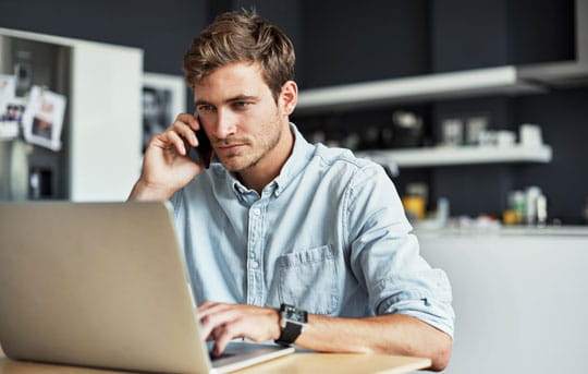 Man talks on cell phone while using laptop