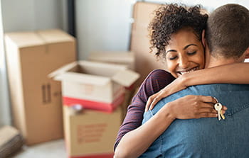Couple hugging with keys in hand and packing boxes 