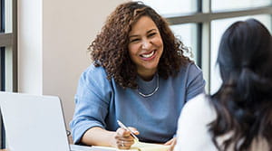 Person smiling at a colleague with notepad on desk
