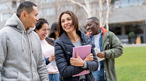 Five college age kids of varying ethnicities walking outdoors on a college campus