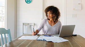 Woman paying bills at kitchen table with laptop